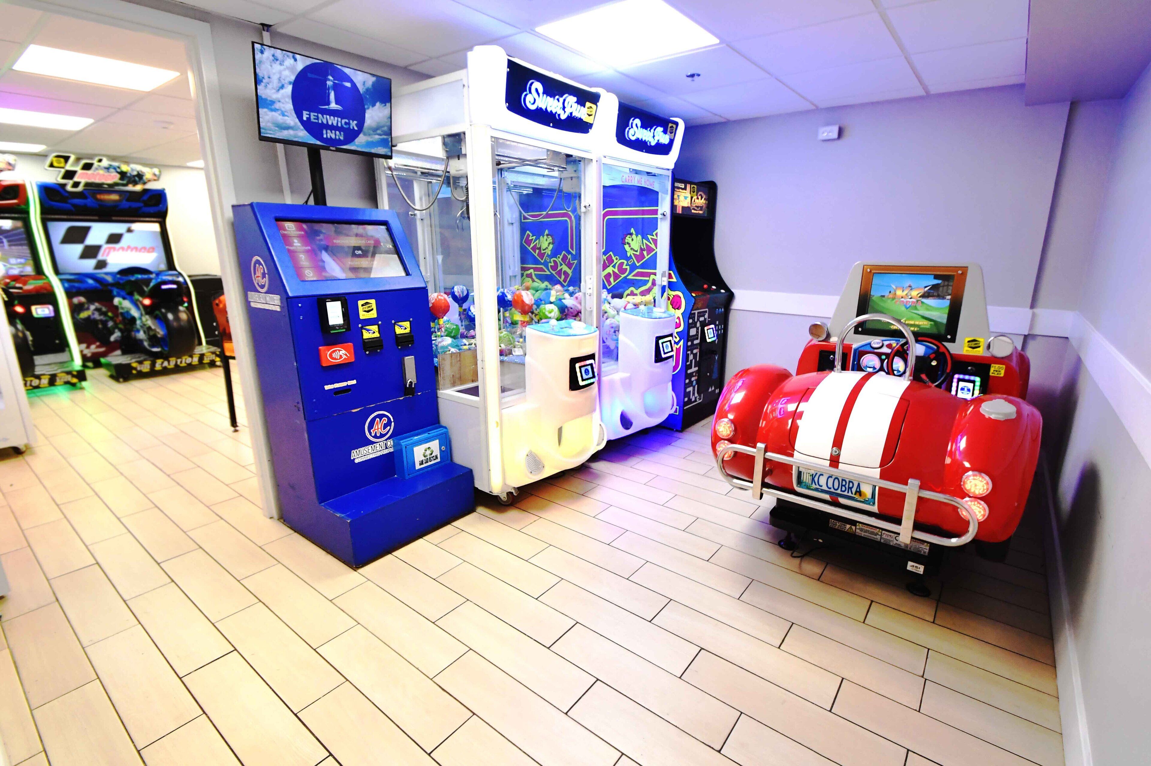 A gaming area with claw machines, a racing simulator, and a television screen displaying a game.