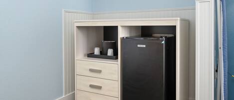 A room with a built-in black refrigerator, a wooden cabinet with drawers, and a blue wall.