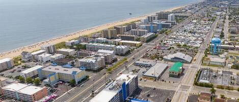 An aerial view of a coastal city with a beachfront, commercial buildings, and a parking lot.