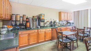 A kitchen with wooden cabinets, a stainless steel sink, and a breakfast bar with various food items and appliances. - Howard Johnson by Wyndham Gillette (Gillette)