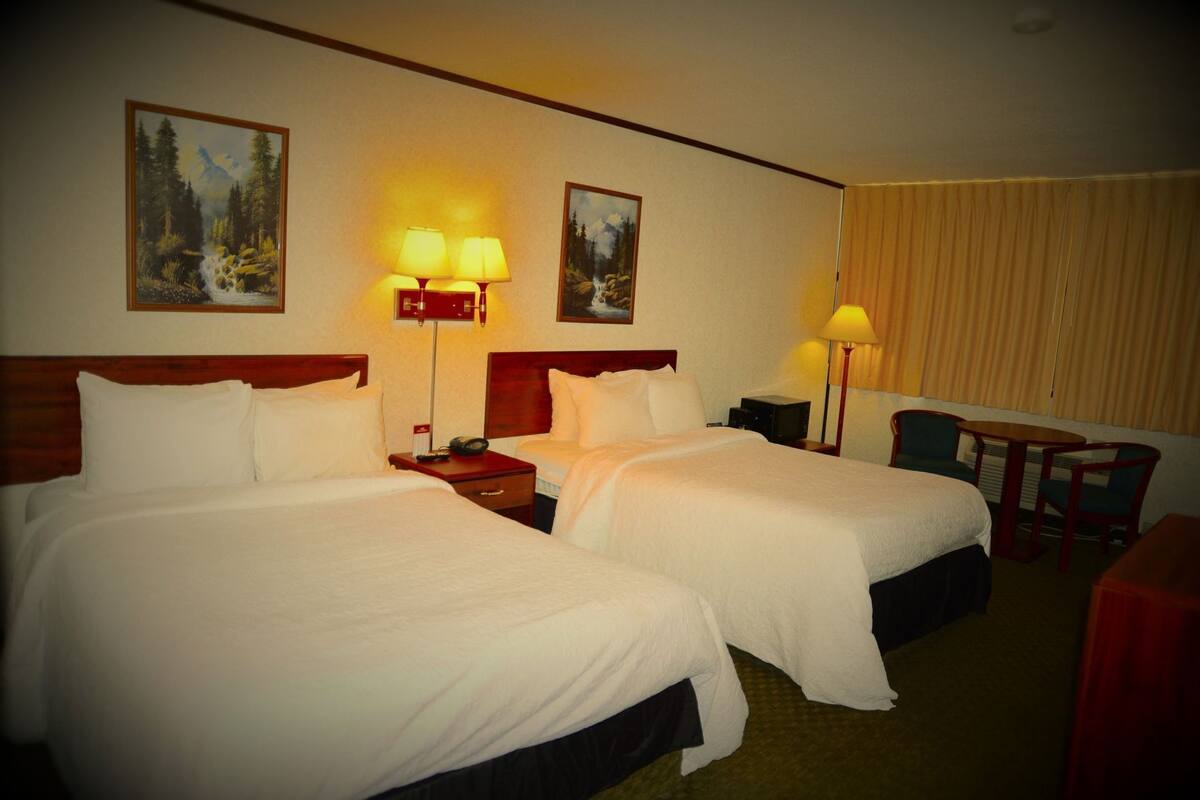 A hotel room with two beds, a desk, a chair, and two lamps.