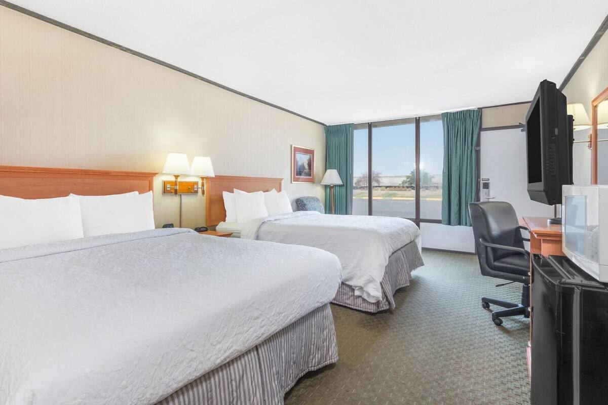 A hotel room with two beds, a desk with a computer, a TV, and a window with curtains.