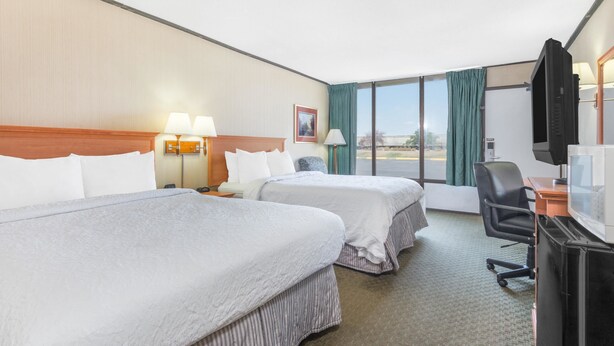 A hotel room with two beds, a desk, a chair, a TV, and a large window with curtains. - Howard Johnson by Wyndham Gillette (Gillette)