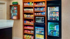 Un hall de hotel con una estación de bebidas de autoservicio, microondas y máquina expendedora.