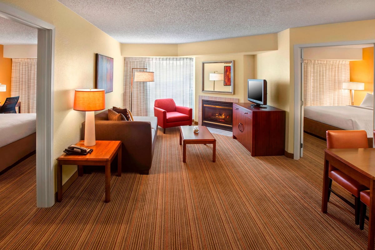 Une chambre d’hôtel avec un lit, un canapé, un fauteuil rouge, une petite table, une télévision, une cheminée et un bureau avec une lampe.