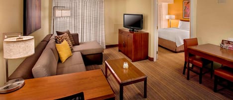 A hotel room with a sofa, a TV, a wooden table, a desk, and a bed.