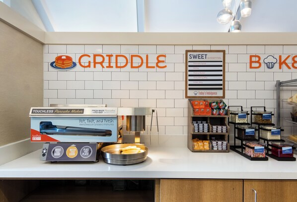 A kitchenette area with a touchless pancake maker, a sign for 'GRIDDLE' with a pancake icon, and a 'SWEET' sign listing various desserts.