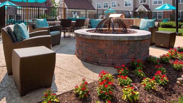 Un patio con mobiliario de mimbre, una chimenea y flores rojas.