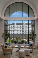 A room with a large arched window, two beige armchairs with blue cushions, a round coffee table, and a patterned rug.
