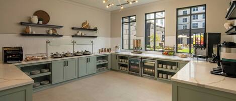 A modern kitchen with light green cabinets, a marble countertop, and a built-in wine cooler. There are shelves with decorative items and a large window providing a view of the outside.