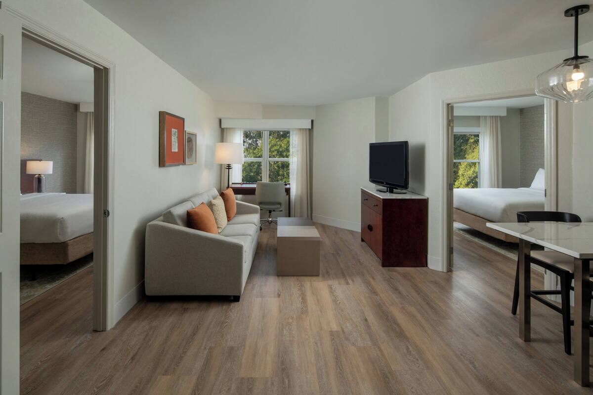 A modern hotel room with a sofa, a TV, a dining table, and a bed.