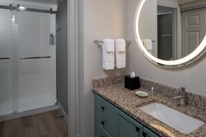 A bathroom with a glass shower enclosure, a granite countertop sink, a mirror with a light, and a towel rack. - Residence Inn by Marriott Atlanta Buckhead (Atlanta)