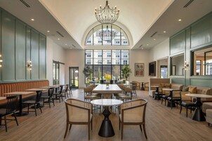 A spacious indoor area with high ceilings, a large chandelier, and multiple seating arrangements including tables and sofas.