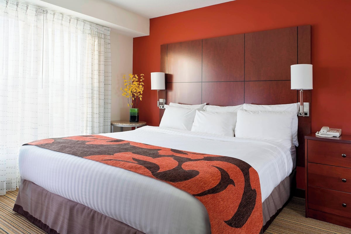 A hotel room with a large bed, two bedside tables, a nightstand, a lamp, and a vase with flowers.