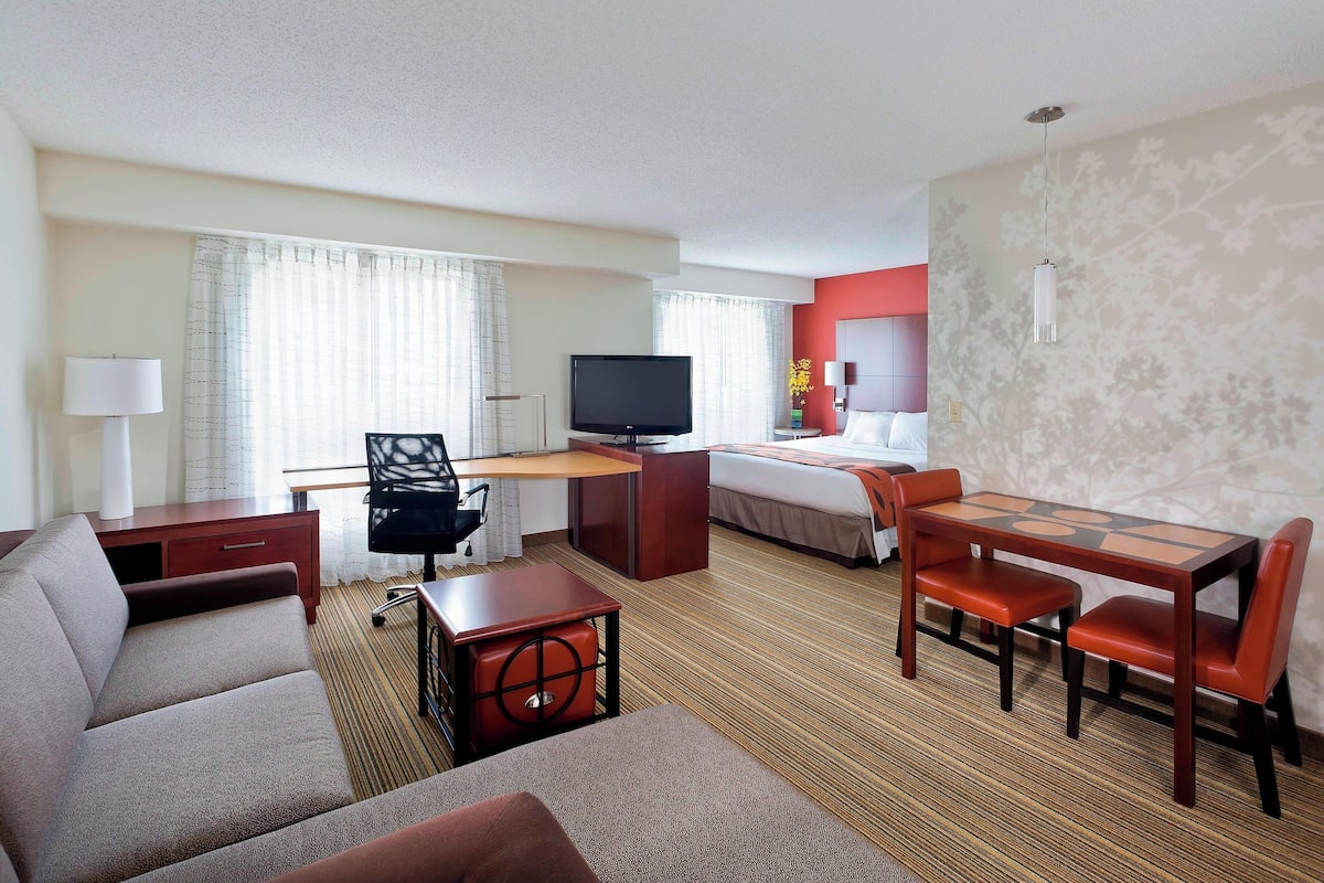 A hotel room with a sofa, a desk with a TV, a bed, and a dining table with chairs.