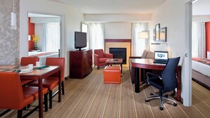 Camera d'albergo con angolo ristoro, televisione, camino, un letto e una scrivania con un portatile.