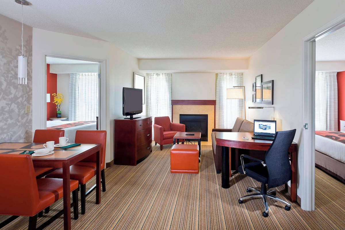 A hotel room with a dining area, a TV, a fireplace, a bed, and a desk with a laptop.