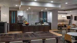 Un comedor de hotel moderno con una isla central, diversas opciones de asientos y una cocina al fondo.