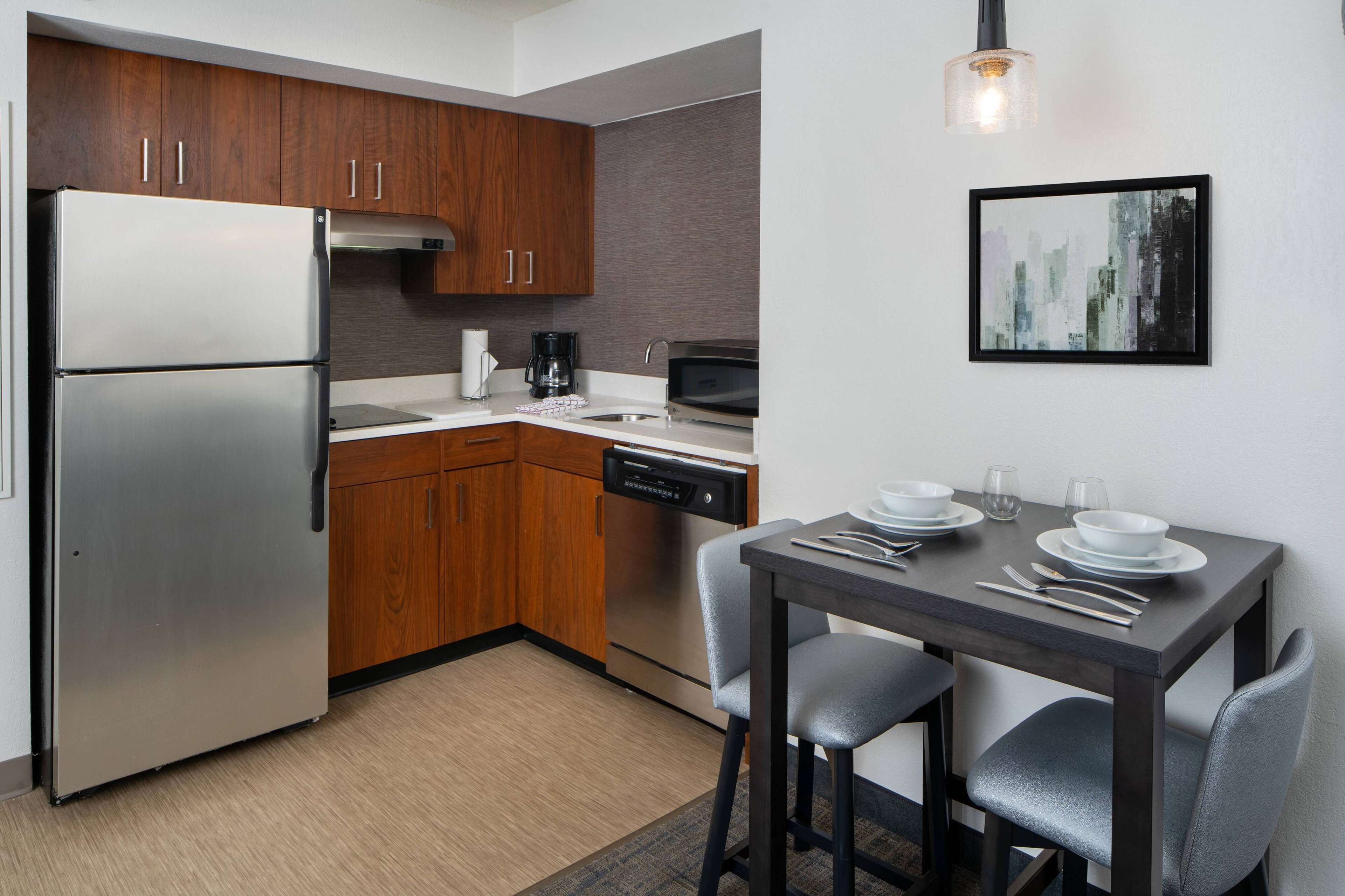 Una cocina moderna con electrodomésticos de acero inoxidable, armarios de madera y una zona de comedor con una mesa y sillas oscuras.