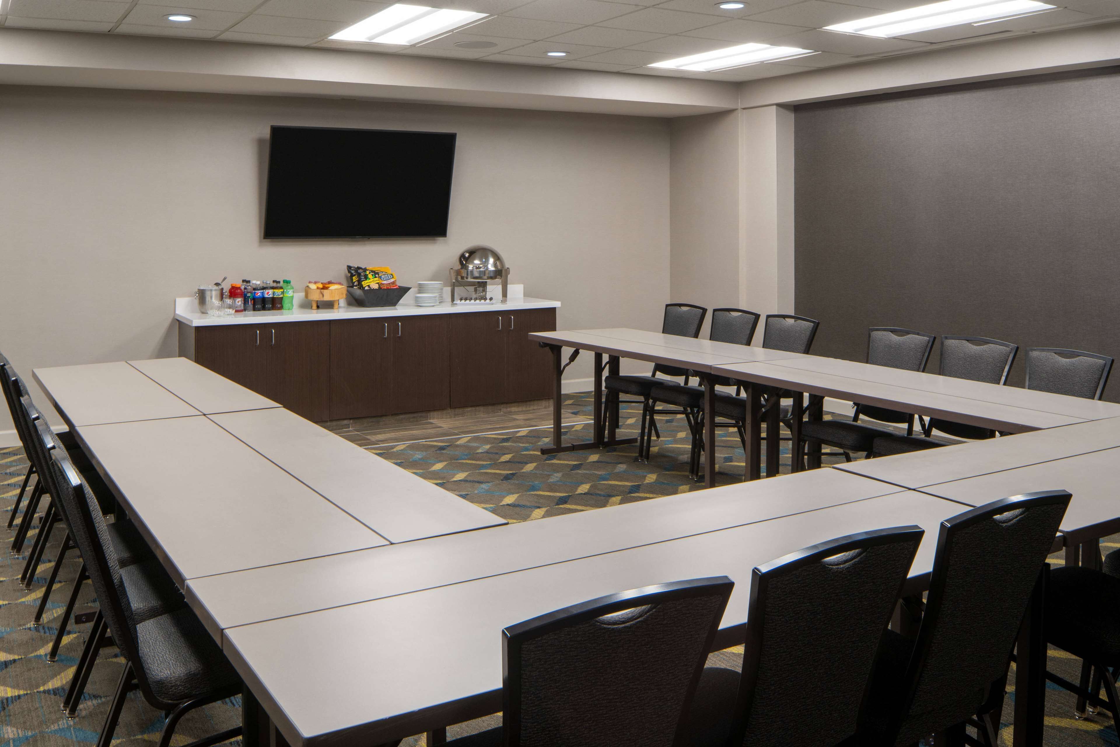 A conference room with a long table, chairs, a projector screen, and a small kitchenette area with snacks.
