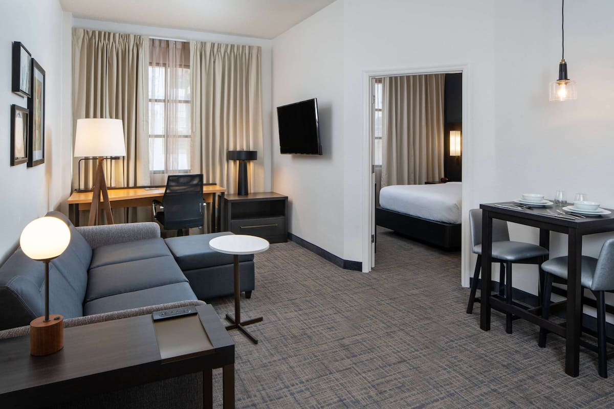 Habitación de hotel con sofá, escritorio, cama, televisor y zona de comedor.
