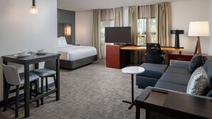 Habitación de hotel con cama, escritorio, sofá, televisor y zona de comedor.