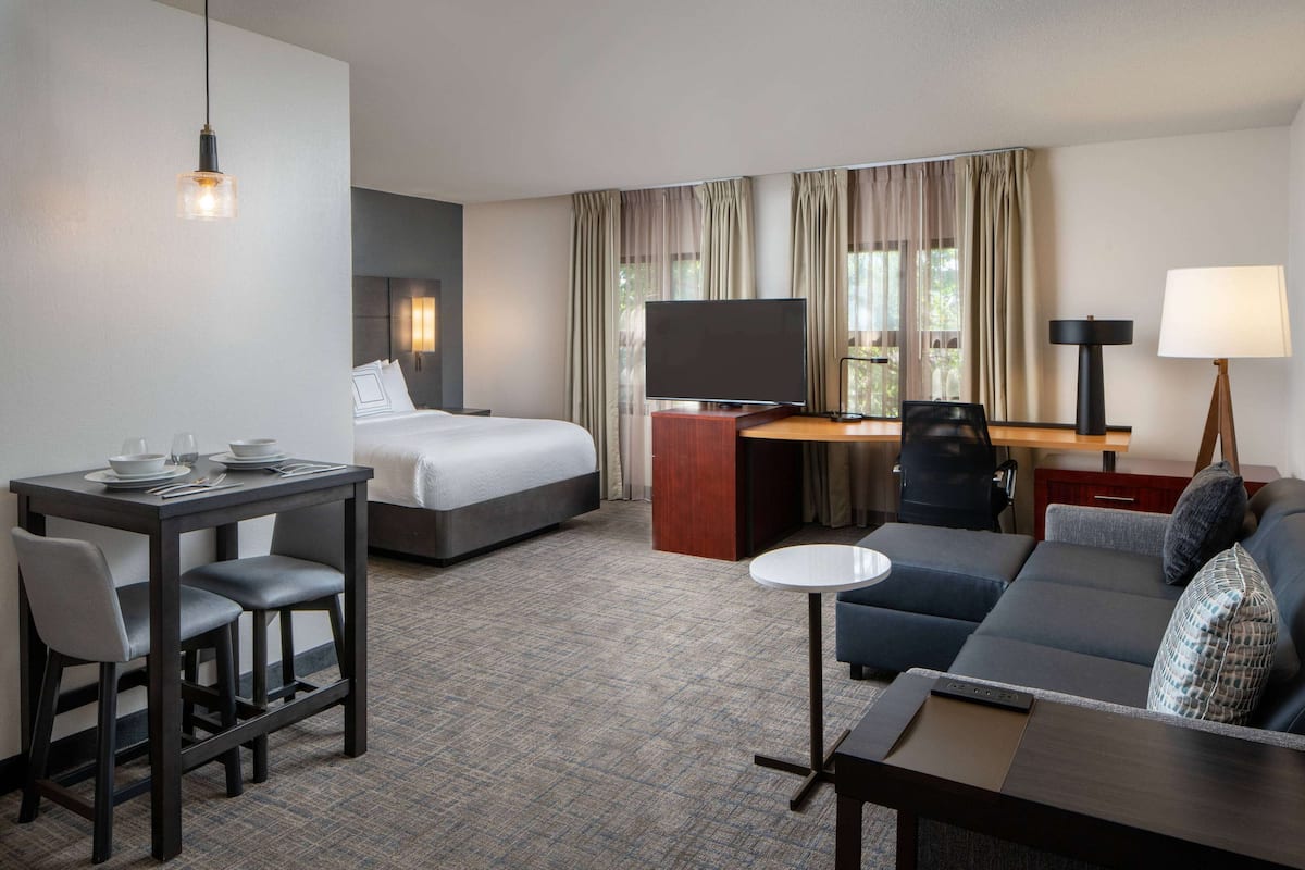 Habitación de hotel con cama, escritorio, sofá, televisor y zona de comedor.