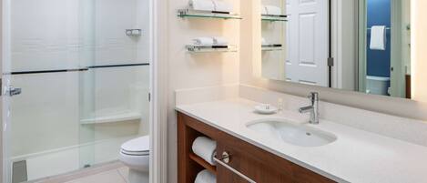 A modern bathroom with a glass shower enclosure, a white toilet, a vanity with a sink and mirror, and towel racks on the wall.