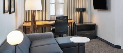 A hotel room with a sofa, a desk, a TV, and a lamp.