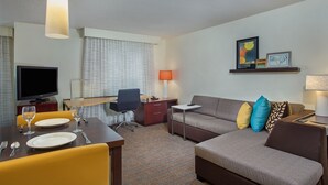 A hotel room with a dining area, a sofa, a TV, and a desk.