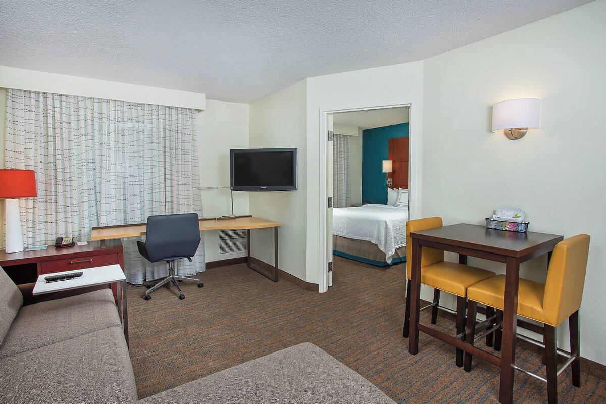 Ein Hotelzimmer mit einem Bett, einem Schreibtisch mit Computer, einem Fernseher, einem Sessel und einem kleinen Tisch.