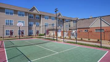 An outdoor tennis court adjacent to a multi-story building with a brick facade.