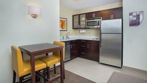 A compact kitchen with dark wooden cabinets, a stainless steel refrigerator, a microwave, and a dining area with yellow chairs.