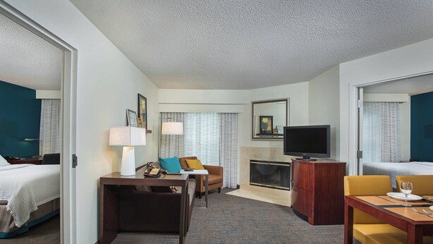 A hotel room with a bed, a desk with a lamp, a chair, a television, and a fireplace.
