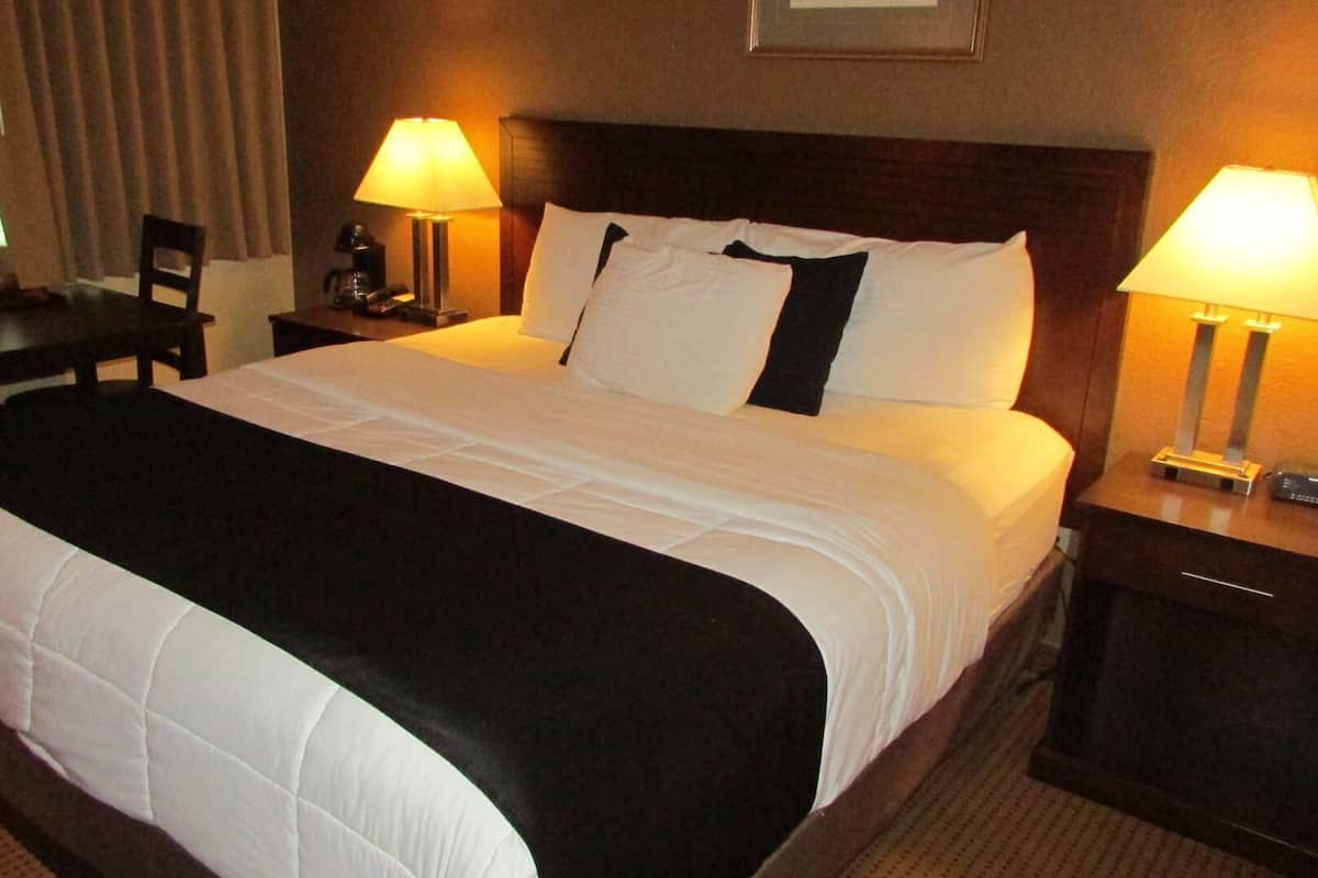 A hotel room with a large bed, two bedside tables with lamps, a chair, and a desk.