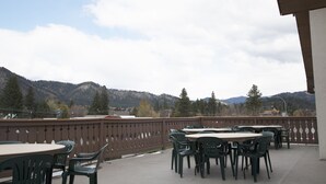 Une terrasse extérieure avec des tables et des chaises, une clôture décorative et une chaîne de montagnes en arrière-plan.