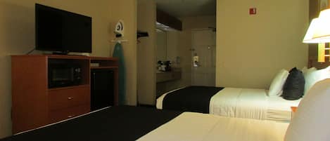 Une chambre d’hôtel avec un téléviseur posé sur un meuble en bois, un lit avec une literie blanche et un petit bureau avec une lampe.