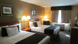 Une chambre d’hôtel avec deux lits, une table de chevet, une lampe, une fenêtre avec des rideaux et un climatiseur fixé au mur.