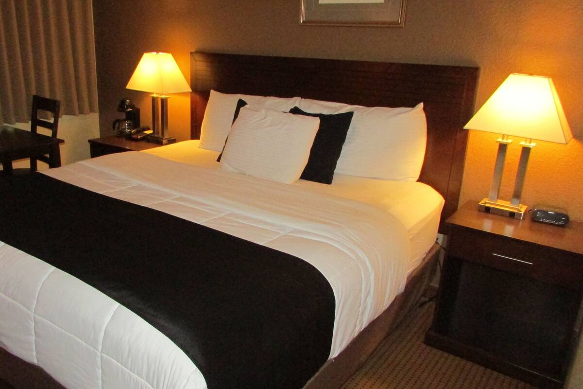 A hotel room with a large bed, two bedside tables with lamps, a desk, and a chair.