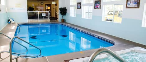 Una piscina interior con agua cristalina, un jacuzzi y una zona de recepción con una planta y cuadros en la pared.