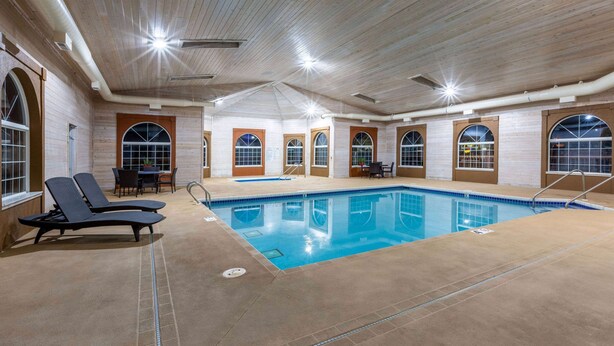 Una piscina interior con sillones de descanso, ventanas arqueadas y suelo de baldosas.