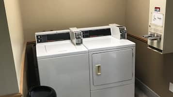 A laundry area with a front-loading washer and dryer, a coin-operated dryer, and a trash can.