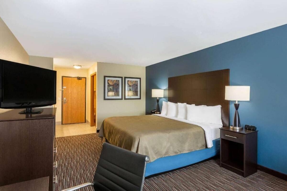 A hotel room with a bed, bedside lamps, a television, a desk, and a chair.