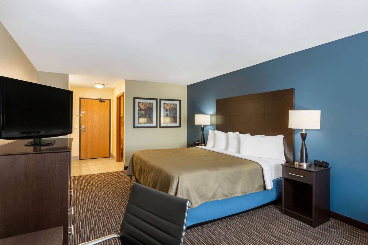 A hotel room with a bed, a desk with a television, a chair, and two bedside lamps.