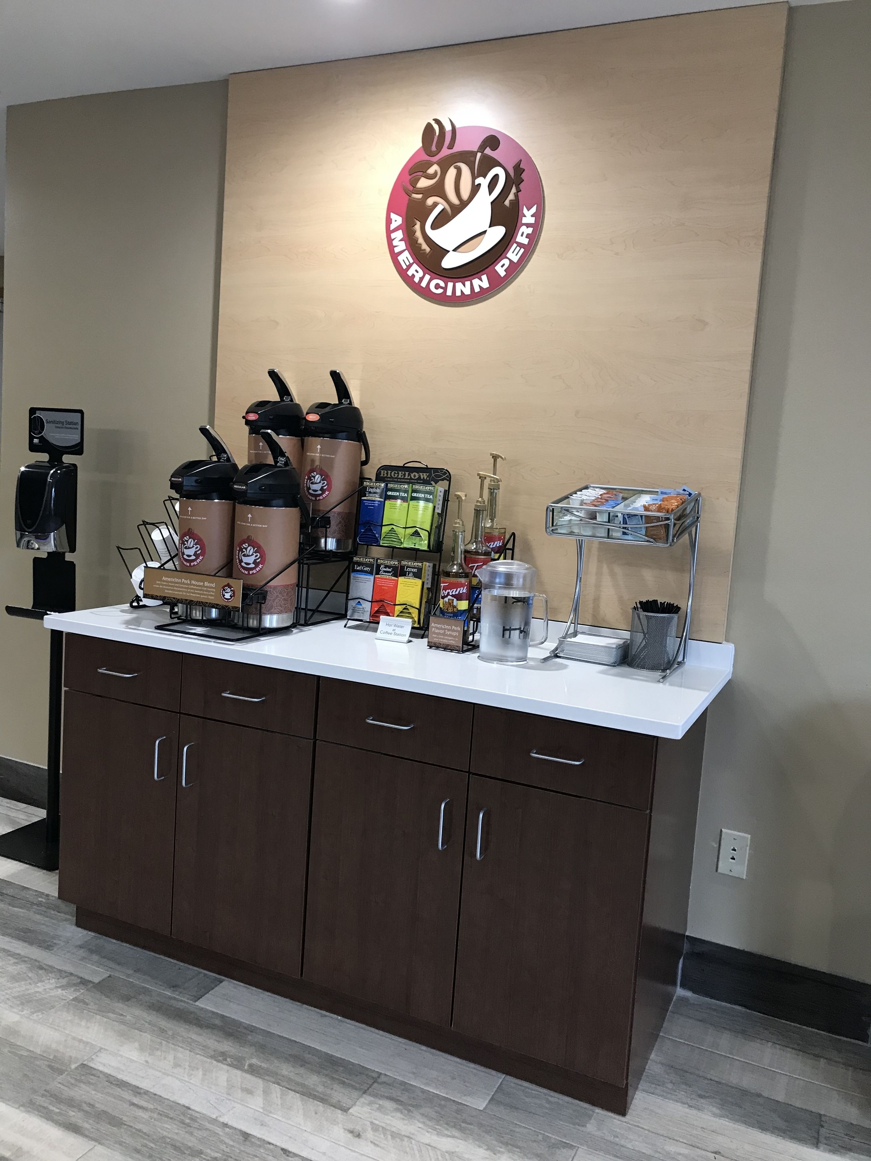 Una estación de café con una máquina de café, dispensadores y una caja de café Bigelow.