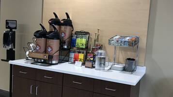Una estación de café con una máquina de café, dispensadores y una caja de café Bigelow.