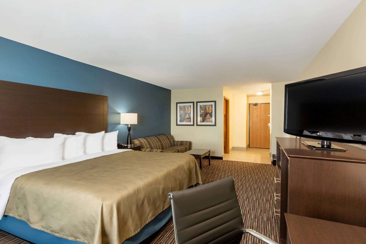 A hotel room with a large bed, a flat-screen TV, a desk, and a sofa.