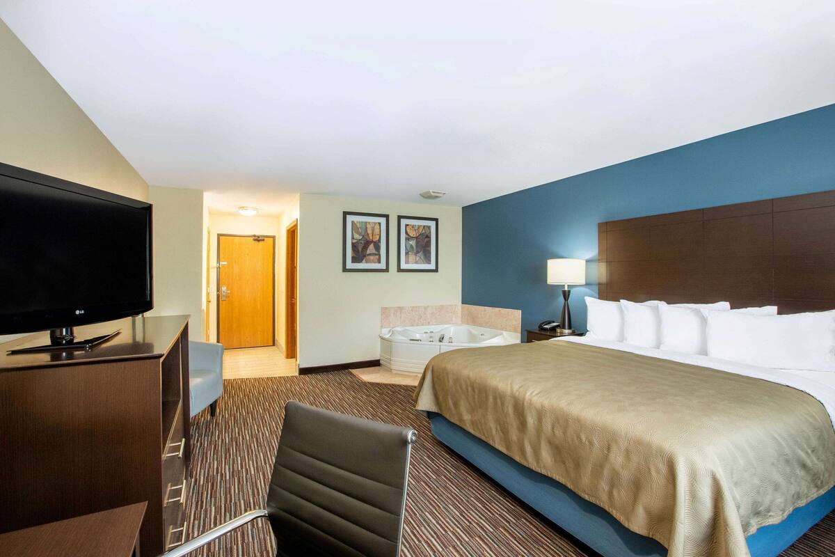 A hotel room with a bed, a TV, a desk, a chair, a bathtub, and two framed pictures on the wall.