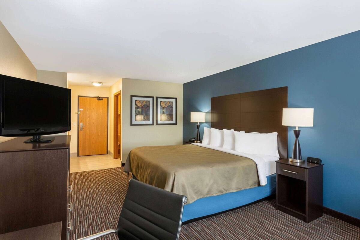 A hotel room with a bed, a desk with a TV, two bedside lamps, and a chair.