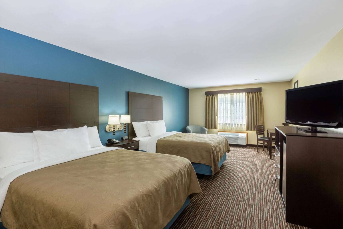 A hotel room with two beds, a TV, a desk, and a chair.